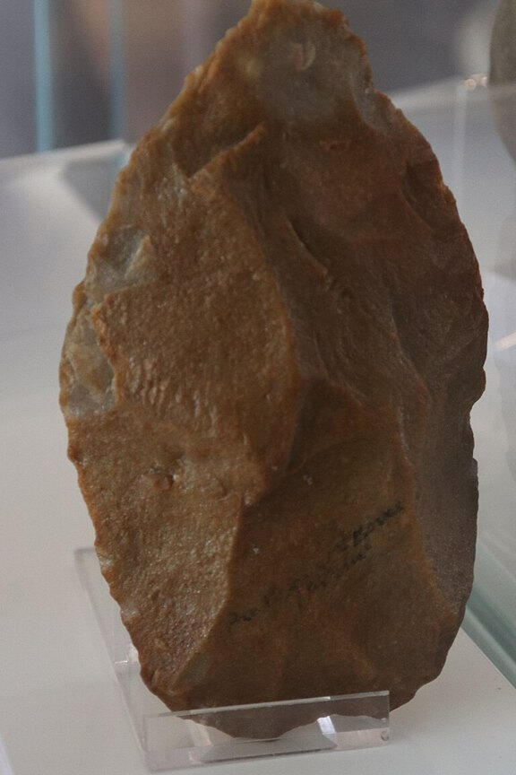 Acheulean flint handaxe on museum display, showing flaked edges and surface detail.